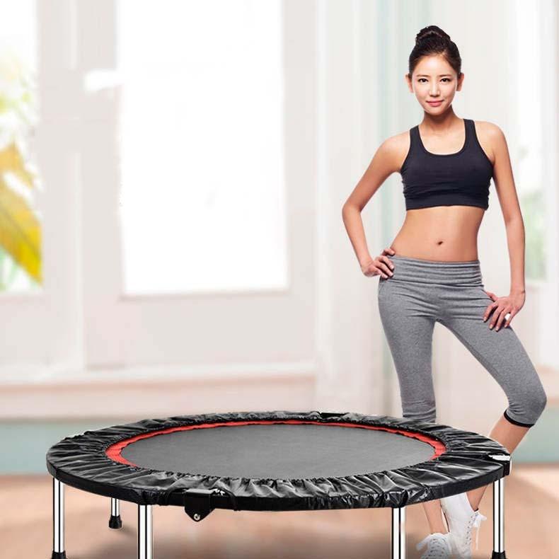 Woman in workout attire standing next to a trampoline indoors