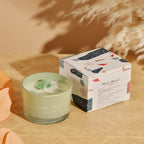 Green scented candle with decorative box on a wooden surface